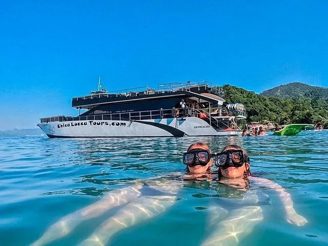 Two people snorkeling in clear water near a large tour boat