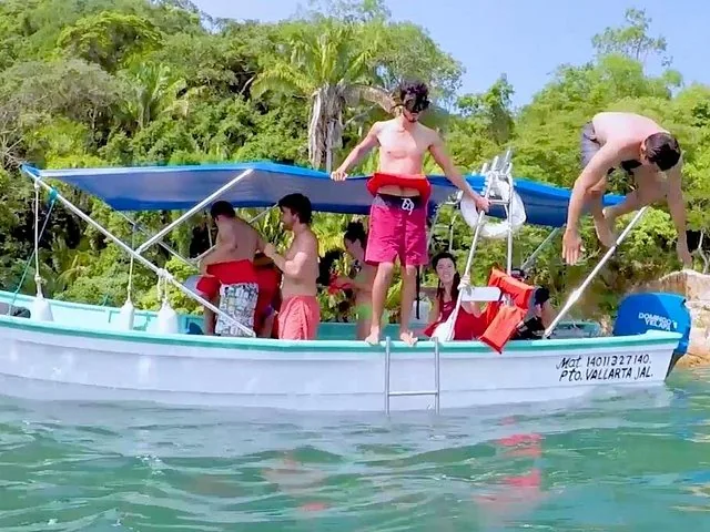 People jumping and playing off a small white boat in the water