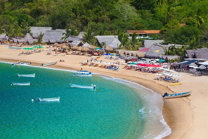 A tropical beach with thatched umbrellas, boats, and people relaxing