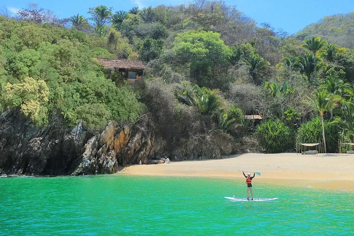 Woman paddleboarding in a vibrant turquoise bay near a rocky, wooded shore